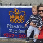 A family pose in front of a knitting celebrating the Jubilee displayed in front of the monument in St Ives.